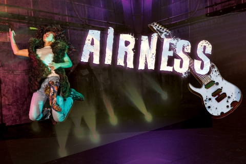Woman jumping into air on stage, with a graphic of a guitar next to her