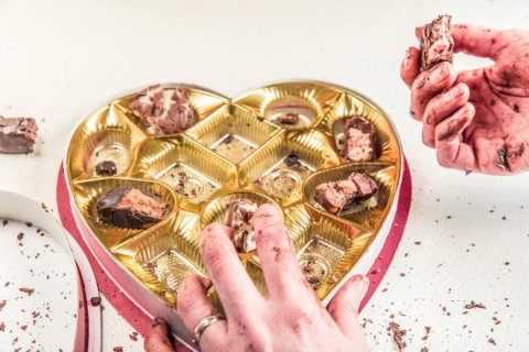 Chocolate-covered hands reaching into a box of candy